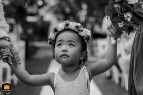 Black and white photo in Avignon of a young flower girl holding the hands of two adults, looking at the groom.